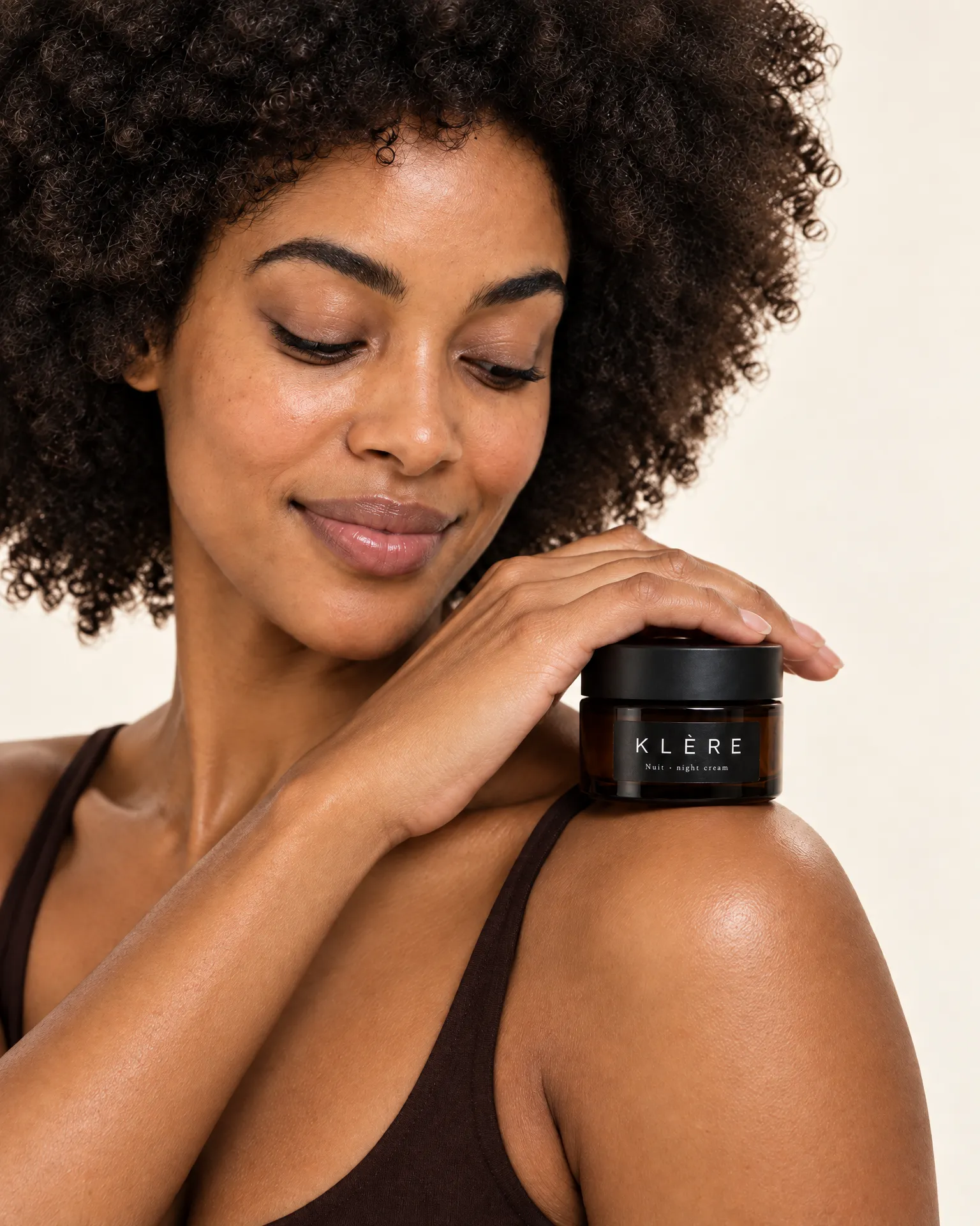 Zuri rests her hand over a jar of Klère Nuit night cream on her bare shoulder.