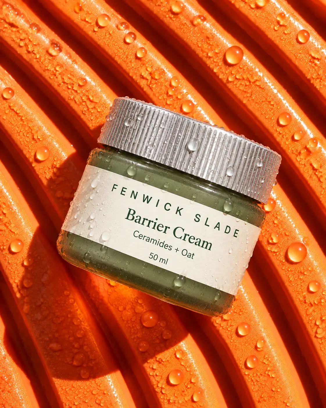 A Fenwick Slade Barrier Cream jar lying on wet orange ribbed rubber, seen from above.