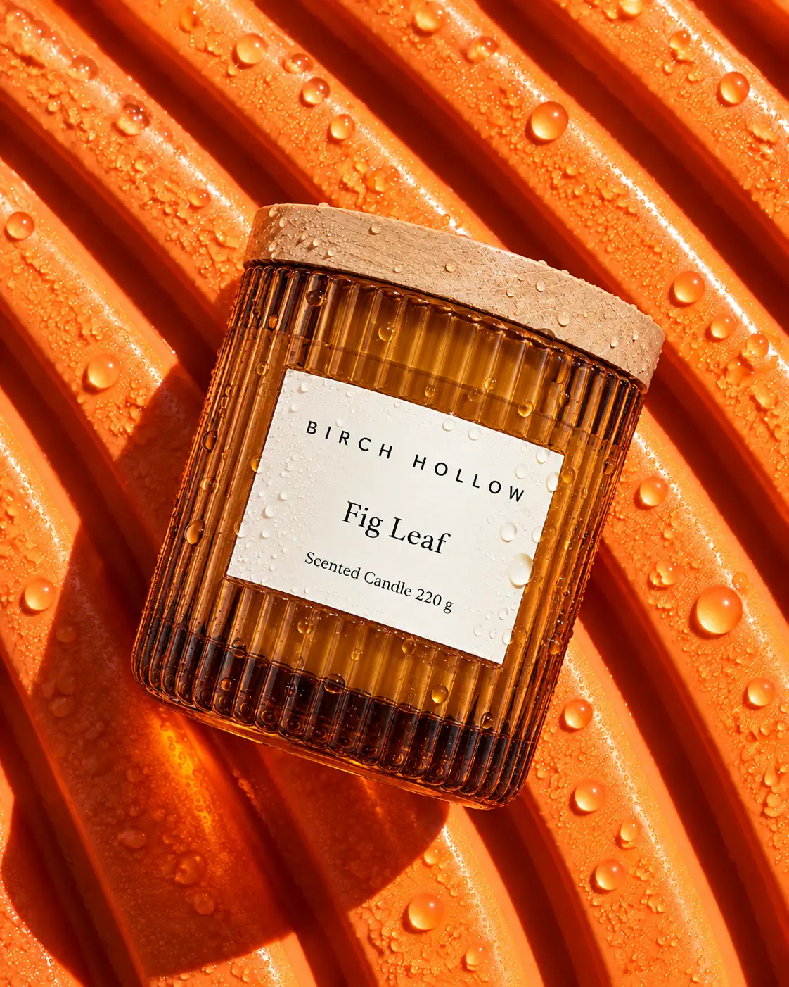 The Birch Hollow Fig Leaf candle lying on wet orange ribbed rubber, seen from above.